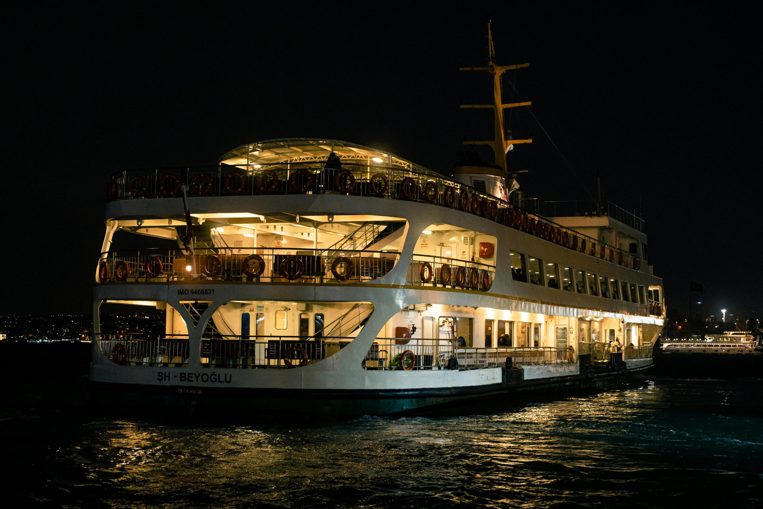 A brightly lit ferry sails through a cityscape at night, creating a vibrant scene.